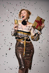 A young woman joyfully posing, surrounded by festive confetti and holding a drink.
