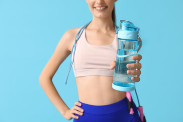 Beautiful young sporty happy woman with bottle of water and jumping rope on blue background, closeup