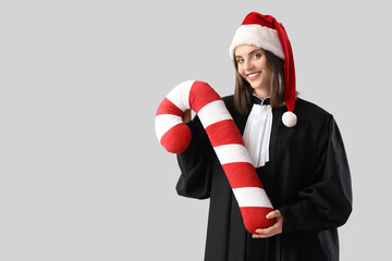 Female judge in Santa hat with candy cane pillow on light background