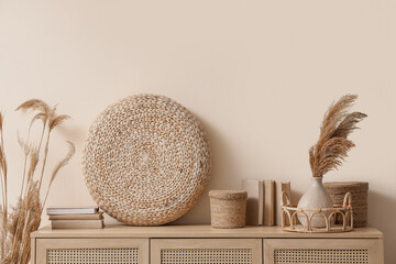 Different home decor and vase of dry reeds on stylish commode near beige wall in room