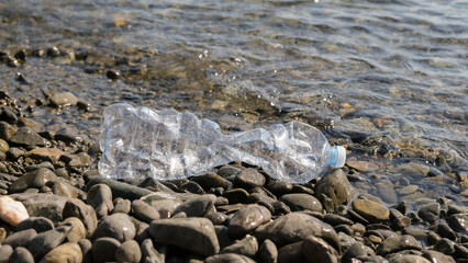 A plastic, transparent, used bottle of drinking water lies on the seashore on a pebble beach. The concept of environmental pollution with plastic waste.