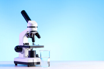 Modern microscope and laboratory flask with liquid on white table