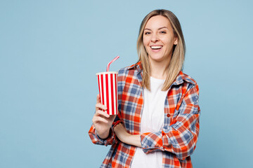 Young smiling happy woman she wear red shirt t-shirt casual clothes hold in hand cup of soda pop drink cola water isolated on plain pastel light blue cyan background studio portrait Lifestyle concept