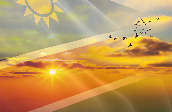 Waving the flag of Namibia against the background of a sunset or sunrise. Namibia flag for Independence Day. The symbol of the state on wavy fabric. - Powered by Adobe