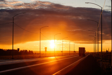 A truck is driving down the road into an orange sunset