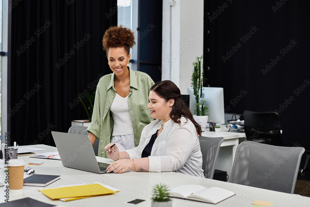 Wall mural two professional women engage in a collaborative discussion over a laptop in an office setting.