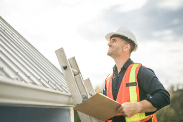 man with hard hat standing on steps inspecting house roof