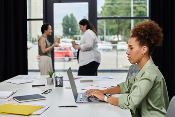 In a modern office, two professionals chat while another works diligently.