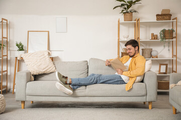 Fototapeta premium Young man reading book on sofa at home
