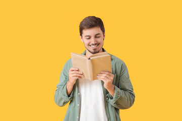 Young man reading book on yellow background