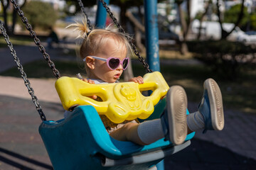 Young child on a swing wearing heart-shaped sunglasses in a sunny playground setting