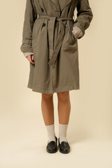 Woman wearing classic green trench coat and black leather moccasins with white socks, autumn fashion items. © triocean