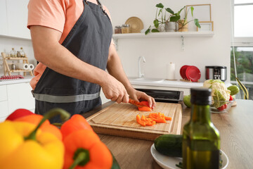 Handsome man cutting bell pepper in kitchen, closeup