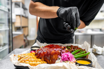 chef in a professional kitchen garnishes a dish of roasted meat with fresh herbs. The focus is on the hands and the beautifully presented dish, highlighting culinary artistry and attention to detail.