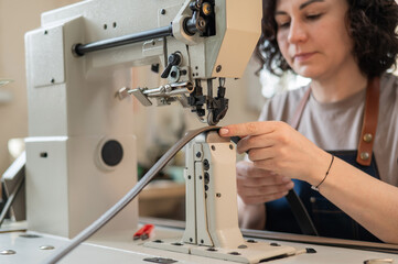 A woman tanner sews a leather belt on a sewing machine. 