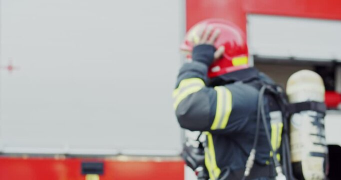 African American young firefighter taking on helmet and getting ready to go for emergency call. Outdoor. Fireman walking to water truck and preparing to drive.