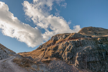 vista panoramica che guarda verso i pendii rocciosi ed erbosi della cima di un monte nel nord Italia, sotto un cielo azzurro, coperto da qualche nuvola leggera e bianca, di giorno, in autunno