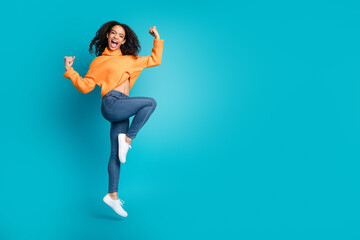 Full length photo of adorable lucky girl orange knitwear jumping high rising fists empty space...