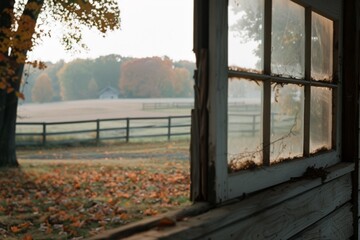 A misty morning view through a weathered window, overlooking a field with distant autumn trees and a wooden fence framing the serene landscape.