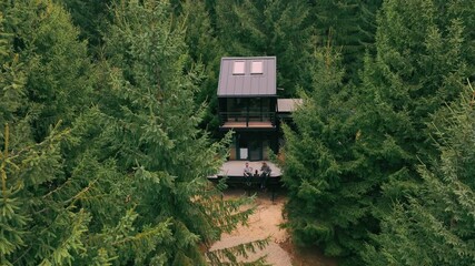 A modern wooden house in the forest among Christmas trees. Two men are drinking tea on a terrace. A cozy house in the forest in the midst of incredible nature