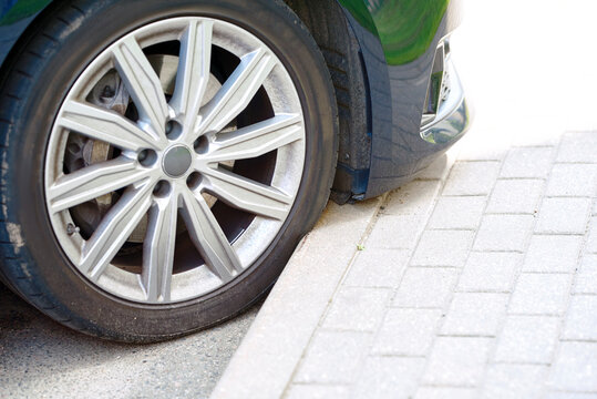 Car tire with bulging sidewall from impact with curb. Car parked close to the curb. Risk of scratching the bumper while parking and damage tire. Low ground clearance