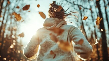 A woman runs through a sunlit forest with leaves swirling around her, capturing the beauty of autumn and the joyful freedom found in movement and nature.