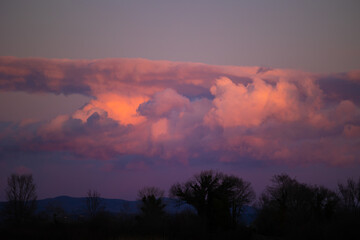 bellissime nuvole dalle sfumature di arancione, rosa e viola, illuminate dalla luce del sole al tramonto, in un ambiente naturale tra pianura e collina, nel nord Italia