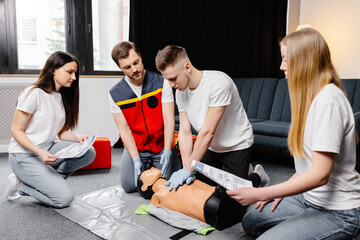Young man instructor helping to make first aid heart compressions with dummy during the group...