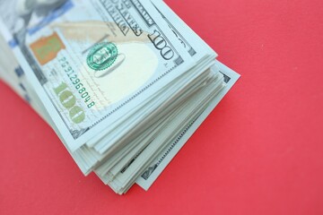 Big amount of hundred dollar bills in thick stack lies on bright red color paper background