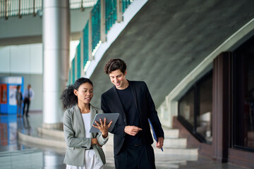 Businessman in black suit walking and discussing with businesswoman in casual suit with tablet...
