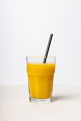 Freshly squeezed orange juice in a glass with a straw. A healthy drink on a light background.