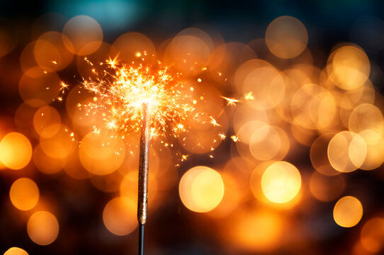Bright sparkler shines brightly against a backdrop of warm, glowing lights during a festive celebration at night