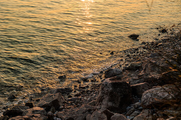 dettagli della marea che lentamente di distende su un bagnasciuga roccioso, mentre il sole al tramonto colora di arancione la superficie del mare