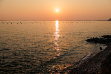 vista panoramica del sole che tramonta sul Mare Adriatico calmo, visto dalla baia di Sistiana, con cielo sereno ed arancione