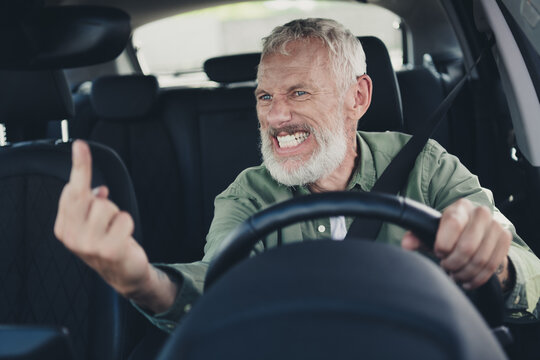 Photo of angry furious mature guy dressed casual shirt riding auto showing fuck you sign outdoors urban city street