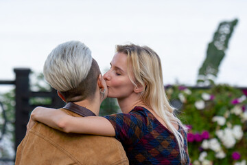 Fototapeta premium a close up beautiful young blonde lesbian couple in summer on bench sitting loving couple enjoying each other hugging kissing looking at camera