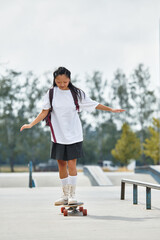 A stylish young Asian girl glides on her skateboard, embodying freedom and youth in a lively park setting.