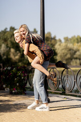 beautiful young blonde lesbian couple in summer walking on the grass girl carries other on her back laughing