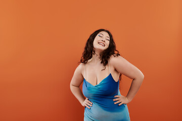 Obraz premium A young woman radiates beauty and confidence in a stunning blue dress, set against a warm orange background.