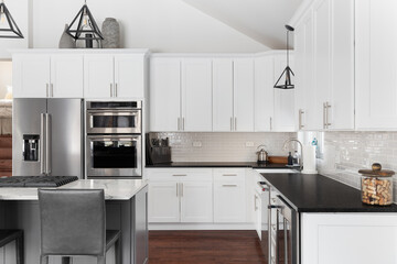 A kitchen with white cabinets, black pendant lights hanging over a grey island, black and white marble countertops, and stainless steel appliances. No brands or labels.