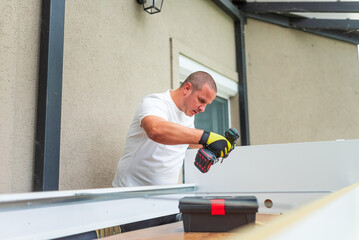 Handyman using cordless drill assembling furniture parts outdoors