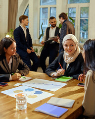 Multicultural female colleagues engaged in discussion during corporate strategy meeting. Other...
