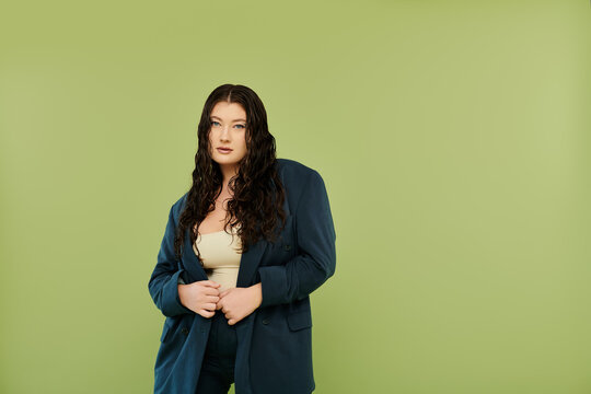 A confident plus-size woman in a fitted suit radiates elegance against a vibrant green background.