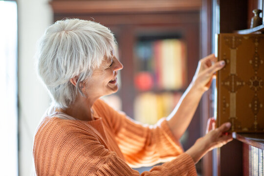 Side view of woman in orange sweater pulling a book from library shelf