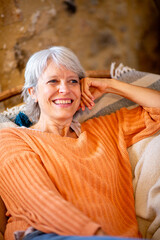 Senior woman smiling while sitting on a couch with an orange sweater