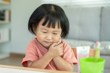 little asian girl presses hand to cheek, suffers from pain in tooth. Teeth decay, dental problems, child emotions and facial expression, oral health care, reducing sweets, fluorine coating