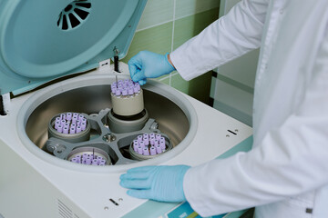 Scientist operating laboratory centrifuge machine, wearing protective gloves and handling test tube...