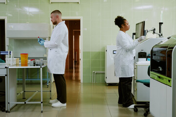 Scientists conducting research in modern laboratory setting, both wearing lab coats and working...