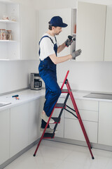 Professional handyman installing kitchen cabinet with electric drill during home renovation, showcasing skilled craftsmanship