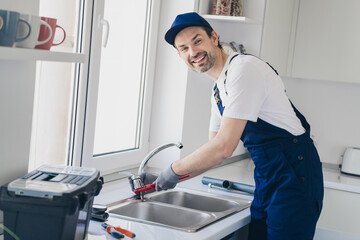 Professional handyman repairing kitchen sink with tools, smiling technician home plumbing perfection in modern apartment setting.